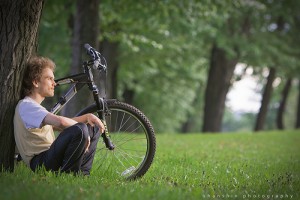young man siting in the park under the tree with a bycicle